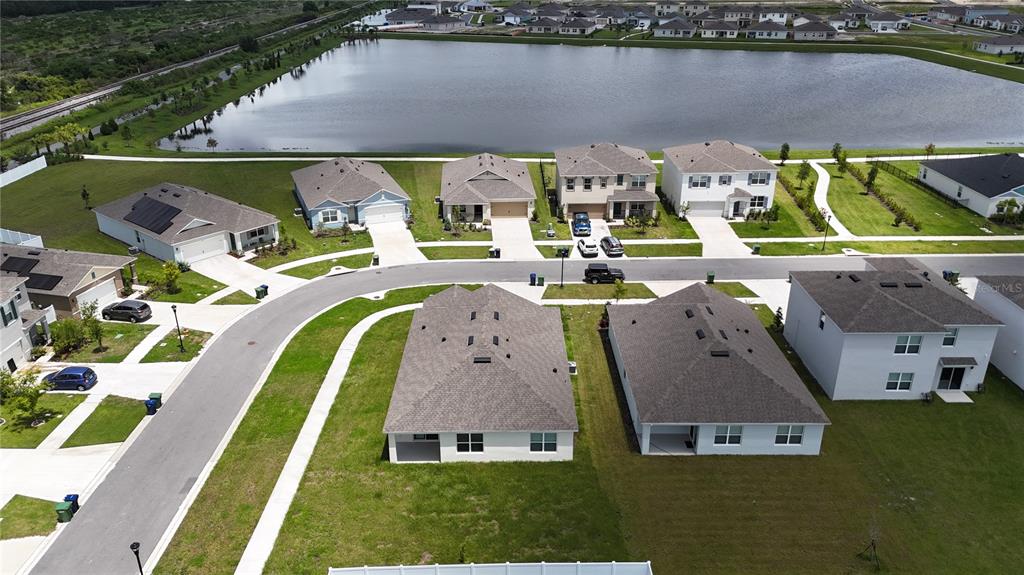 An aerial view shows several suburban houses with gray roofs situated near a large pond — 1340 DAISY FIELD DR, WINTER HAVEN, FL