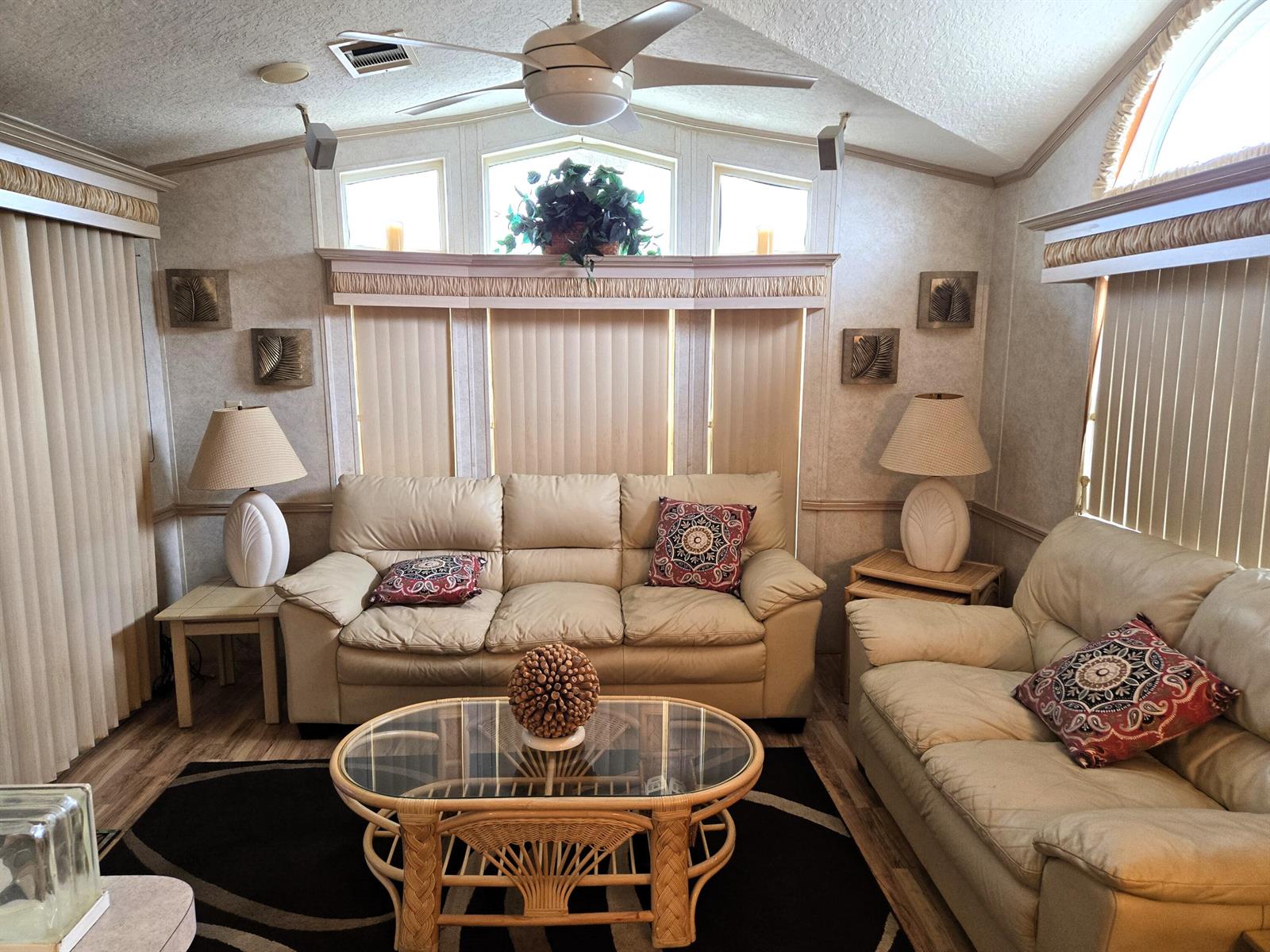 A living room features two beige sofas, a glass-topped rattan coffee table, and vertical blinds — 7950 Hwy 78 W # 314, Okeechobee FL 34974, OKEECHOBEE, FL