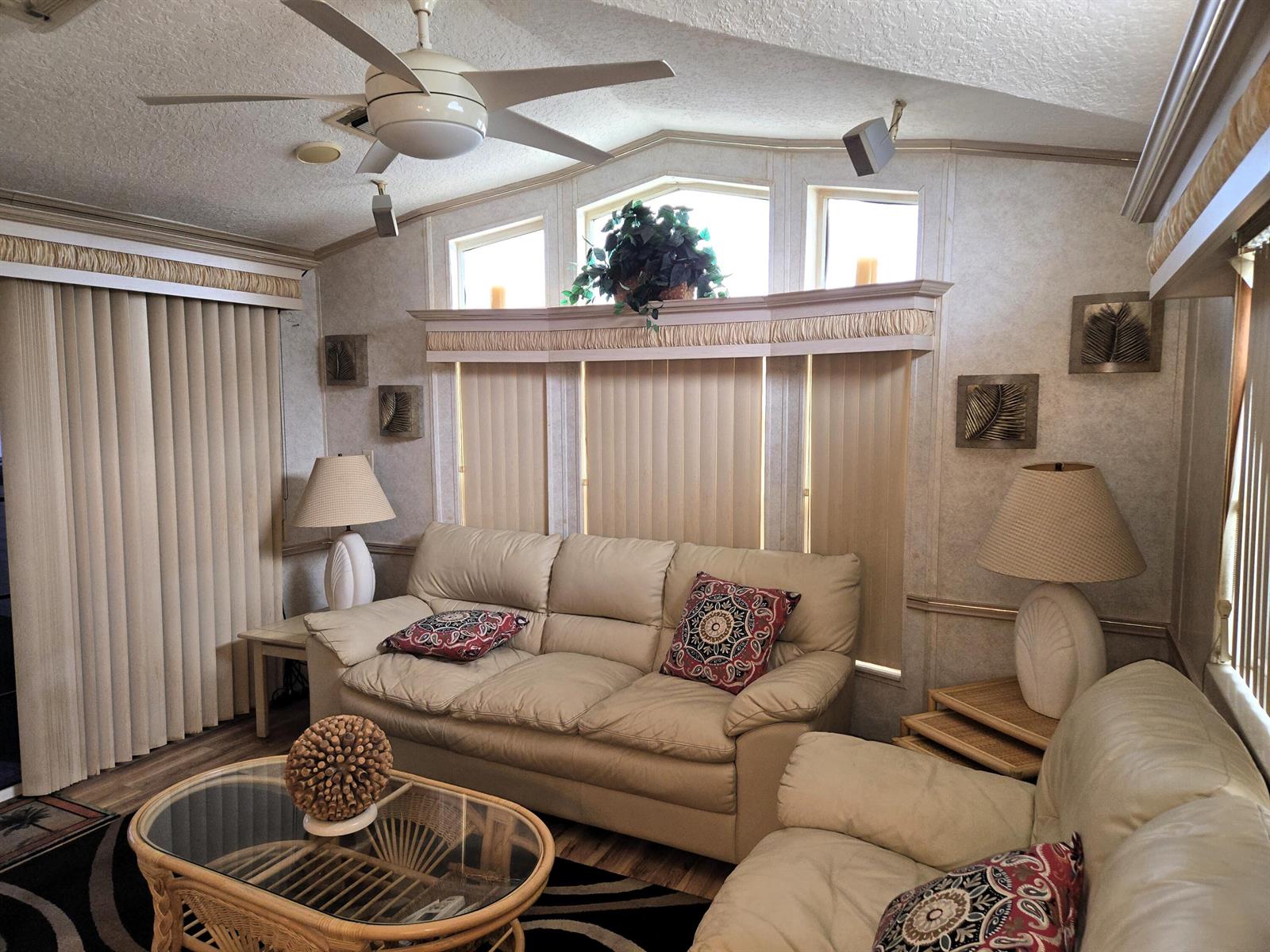 A living room features a beige sofa, a glass-top rattan coffee table, and vertical blinds — 7950 Hwy 78 W # 314, Okeechobee FL 34974, OKEECHOBEE, FL