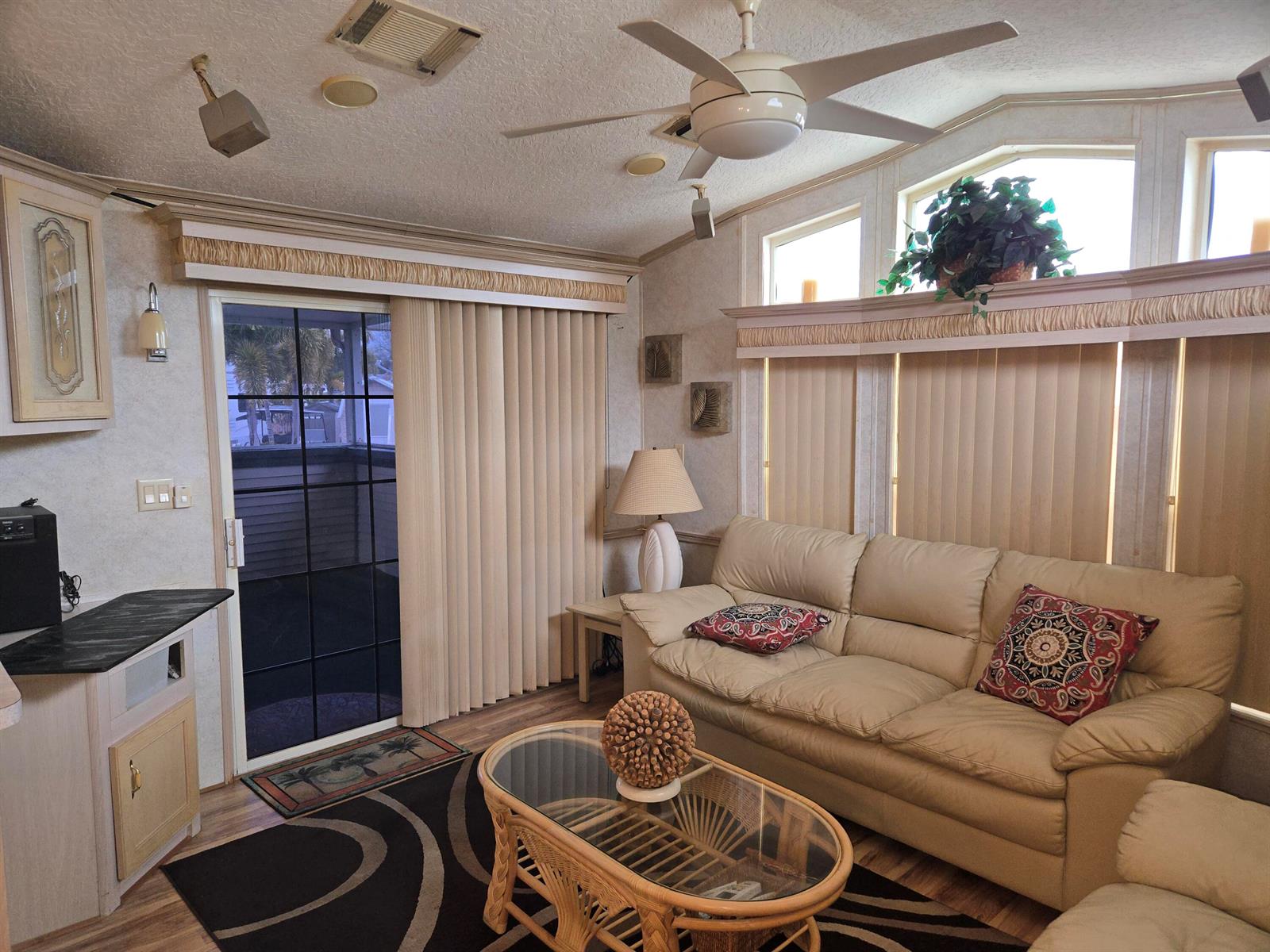 A living room features a beige sofa, glass coffee table, ceiling fan, and vertical window blinds — 7950 Hwy 78 W # 314, Okeechobee FL 34974, OKEECHOBEE, FL