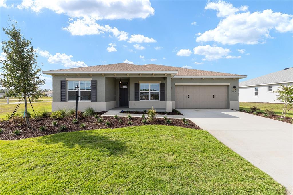 A single-story house with a tan stucco exterior, a two-car garage, and a front lawn — 10731 SW 102ND LANE, OCALA, FL