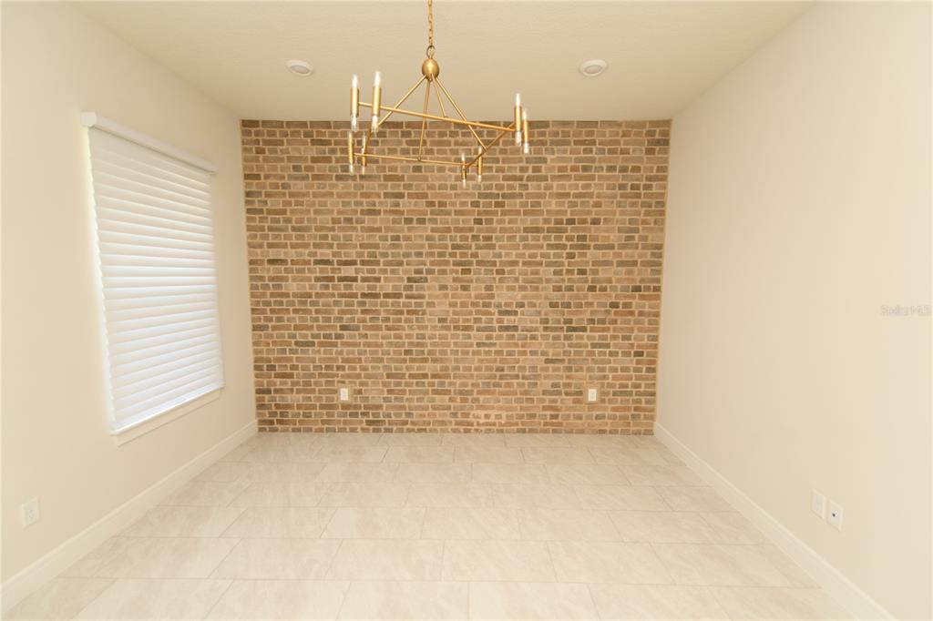 A dining room features a brick accent wall, tile flooring, and a modern gold chandelier — 10746 PAHOKEE BEACH PLACE, ORLANDO, FL