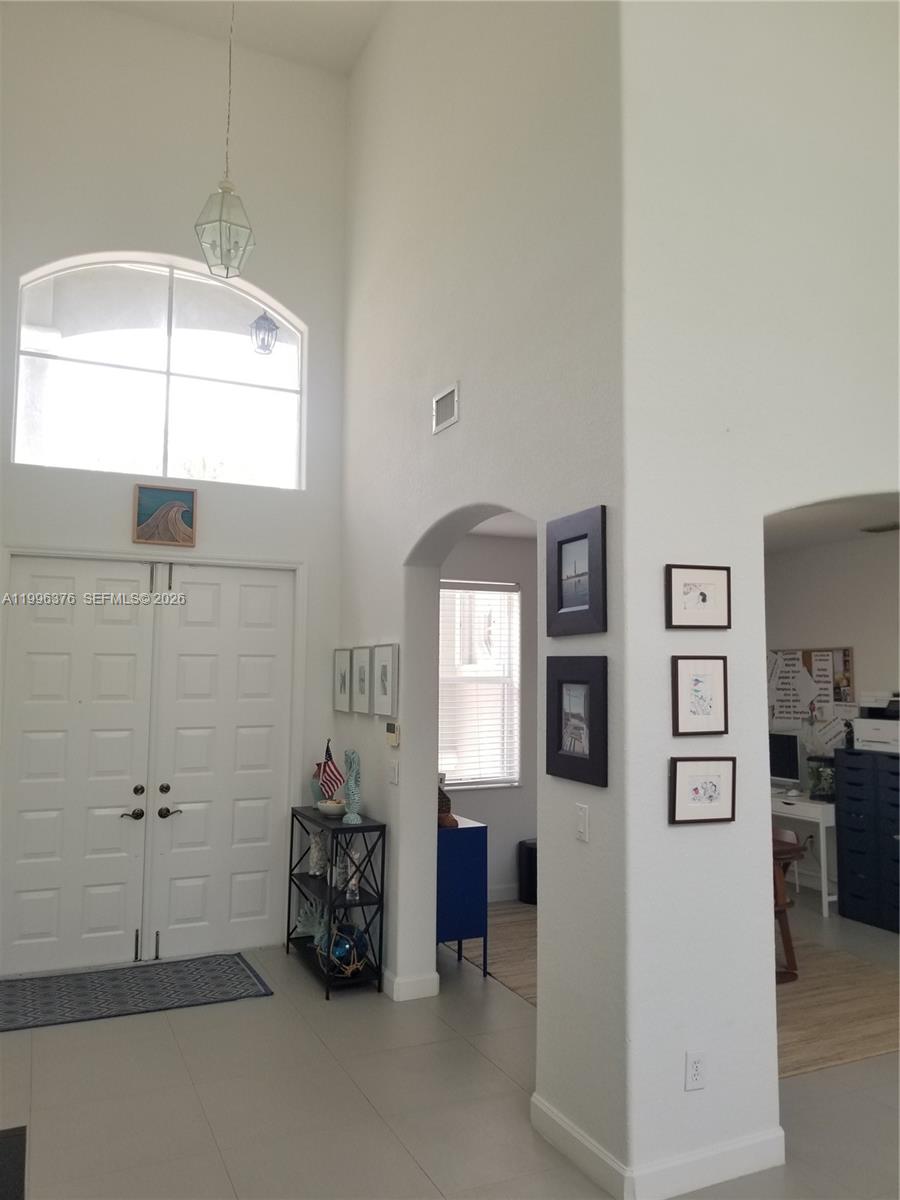 A high-ceilinged entryway features white double doors, tiled floors, and arched doorways leading to other rooms — 4719 NW 96th Pl, Doral FL 33178, DORAL, FL