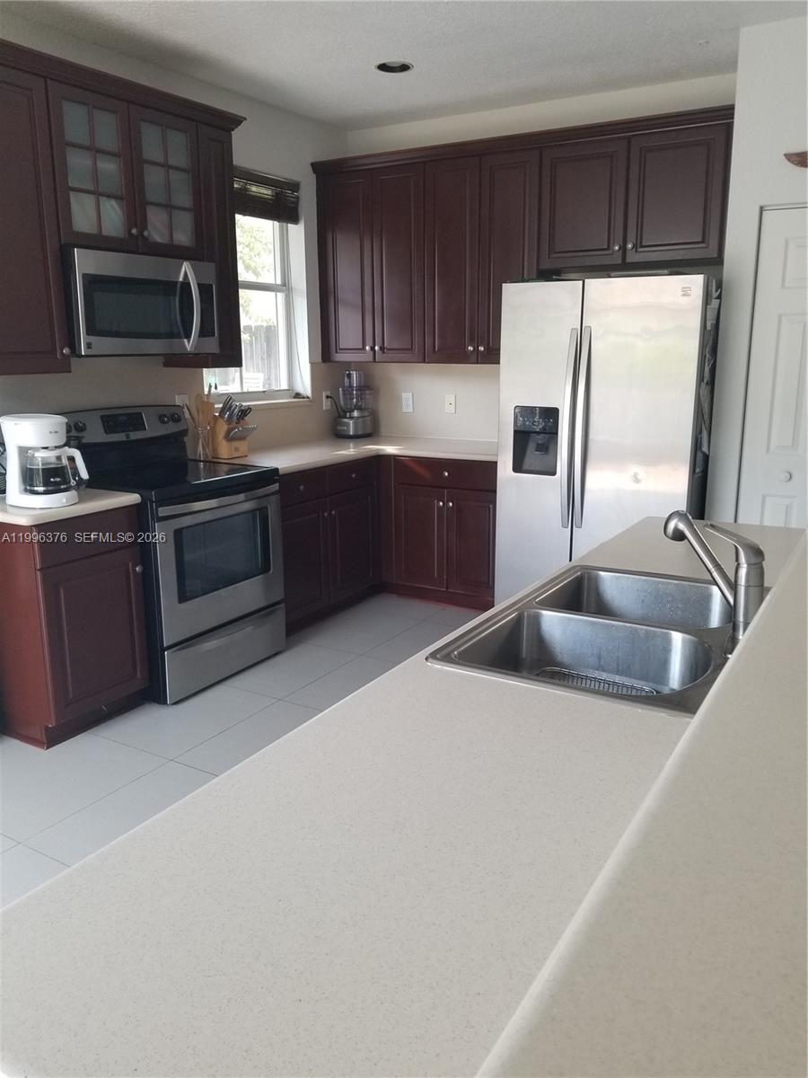 A kitchen features dark wood cabinets, stainless steel appliances, and a light-colored countertop — 4719 NW 96th Pl, Doral FL 33178, DORAL, FL