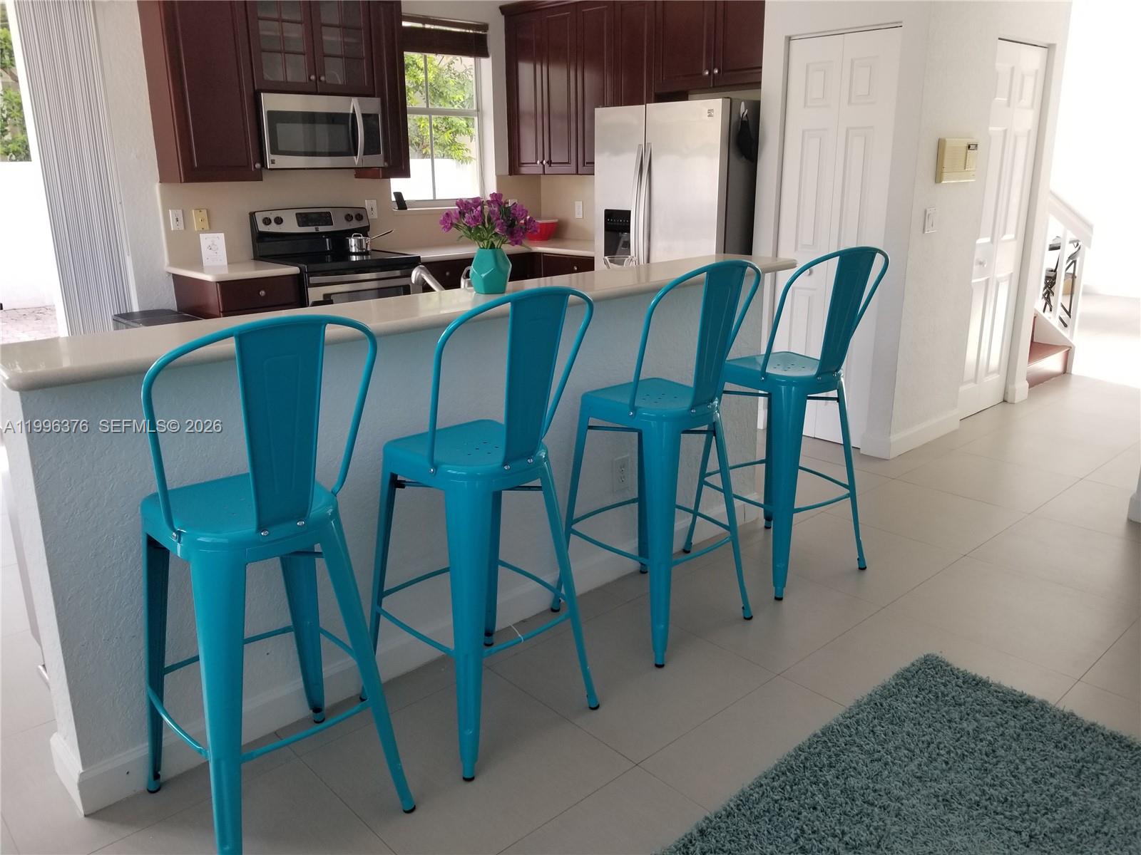 A kitchen features dark wood cabinets, stainless steel appliances, and four bright blue metal barstools — 4719 NW 96th Pl, Doral FL 33178, DORAL, FL