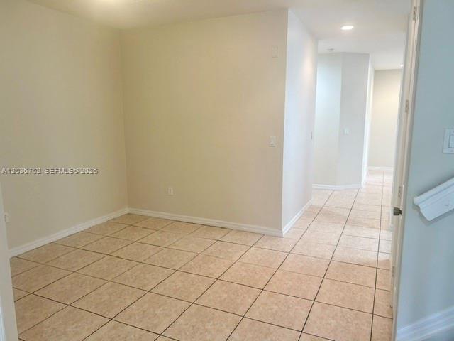 An empty room features beige tile flooring and light-colored walls leading to a hallway — 568 NE 35th Ave, Homestead FL 33033, HOMESTEAD, FL