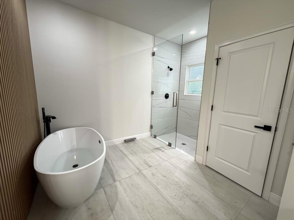 A modern bathroom features a freestanding white tub, a glass-enclosed shower, and light tile flooring — 351 TENK STREET, PORT CHARLOTTE, FL