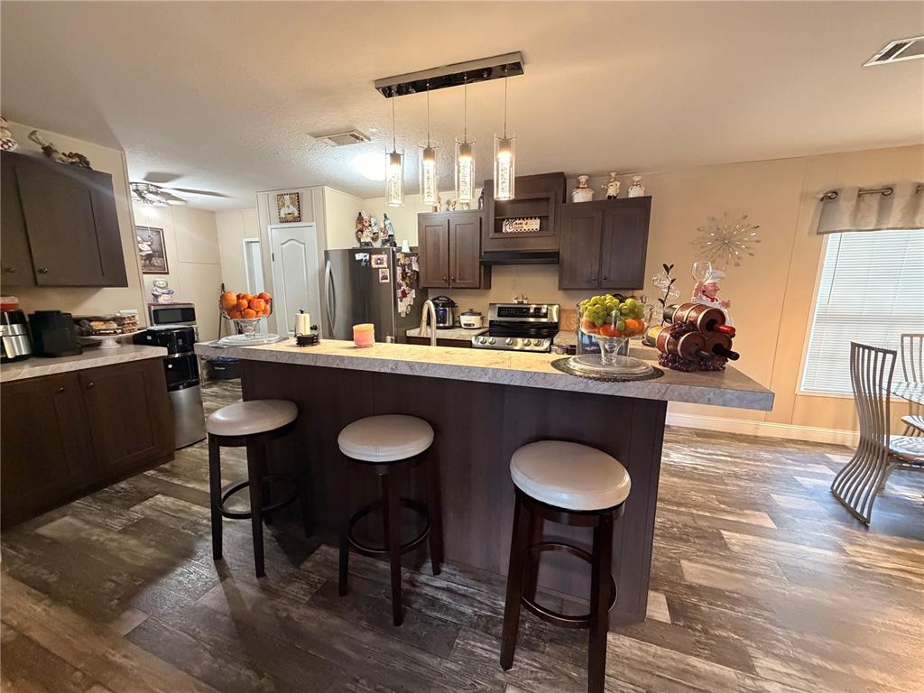 A kitchen features dark wood cabinets, a breakfast bar with three stools, and wood-look flooring — 25408 ONEAL ROAD, BROOKSVILLE, FL