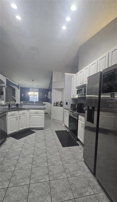 A kitchen features white cabinets, stainless steel appliances, granite countertops, and gray tiled flooring — 3220 ABIAKA DRIVE, KISSIMMEE, FL