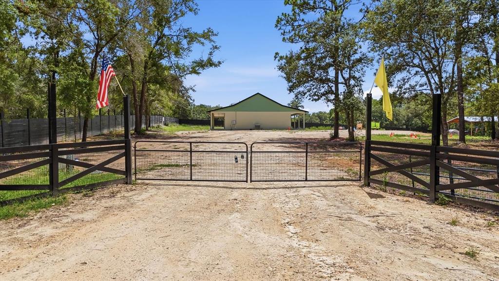 A gravel driveway leads through a metal gate toward a building with a green roof — 5970 W INLAND, DUNNELLON, FL
