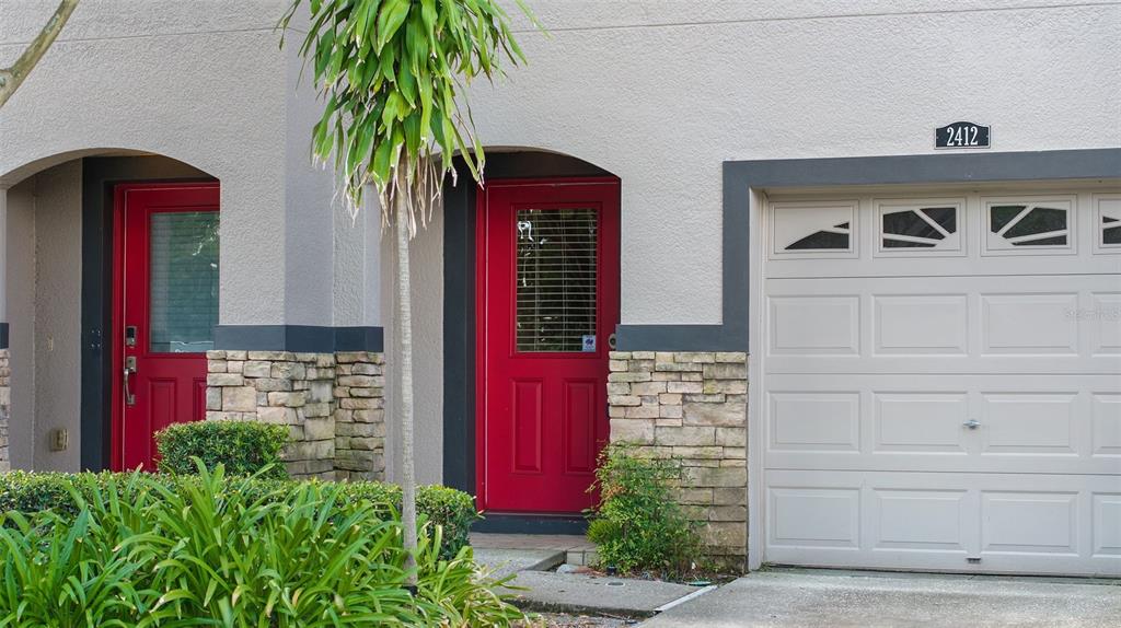 A townhouse exterior features two red doors, stone accents, and a white garage door — 2412 MIDDLETON GROVE DRIVE, BRANDON, FL