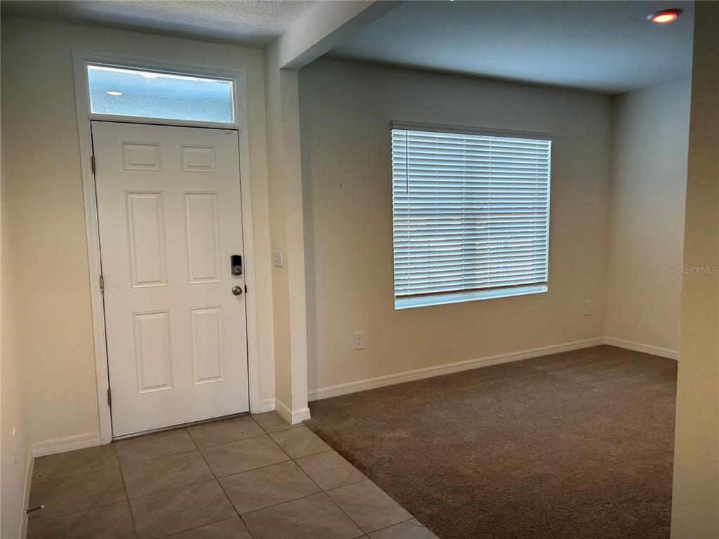 An entryway with tile flooring leads to a carpeted living area with a large window — 17218 RESERVA DRIVE, BRADENTON, FL