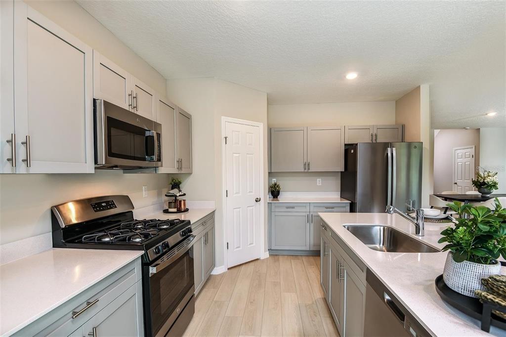 A kitchen features light gray cabinets, stainless steel appliances, white countertops, and wood-look flooring — 36645 SAGEMOOR DRIVE, ZEPHYRHILLS, FL