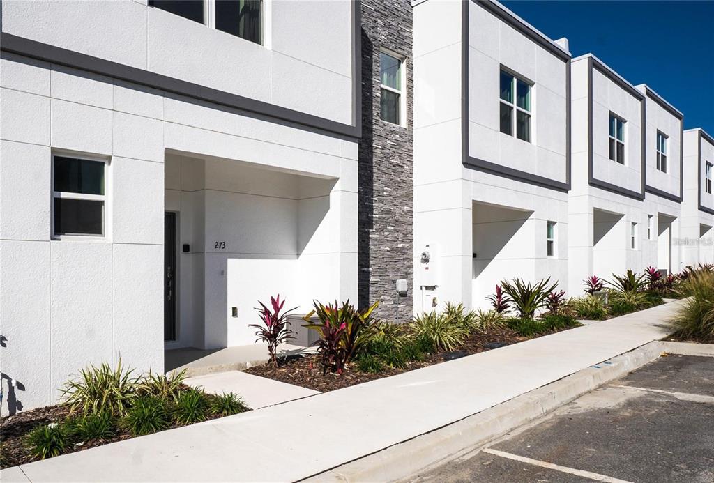 A row of modern townhomes with white stucco facades, stone accents, and small front gardens — 392 FAMAGUSTA DRIVE, DAVENPORT, FL