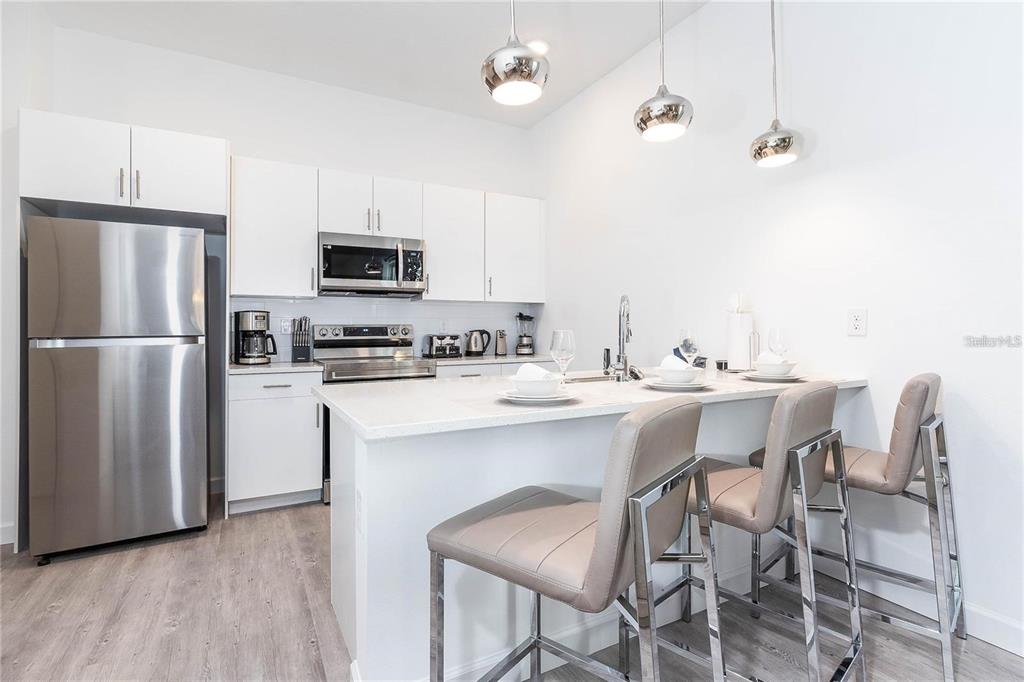 A modern kitchen features white cabinetry, stainless steel appliances, and a breakfast bar with stools — 392 FAMAGUSTA DRIVE, DAVENPORT, FL