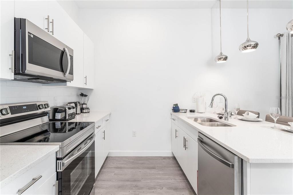 A modern kitchen features white cabinets, stainless steel appliances, and a quartz-topped island — 392 FAMAGUSTA DRIVE, DAVENPORT, FL