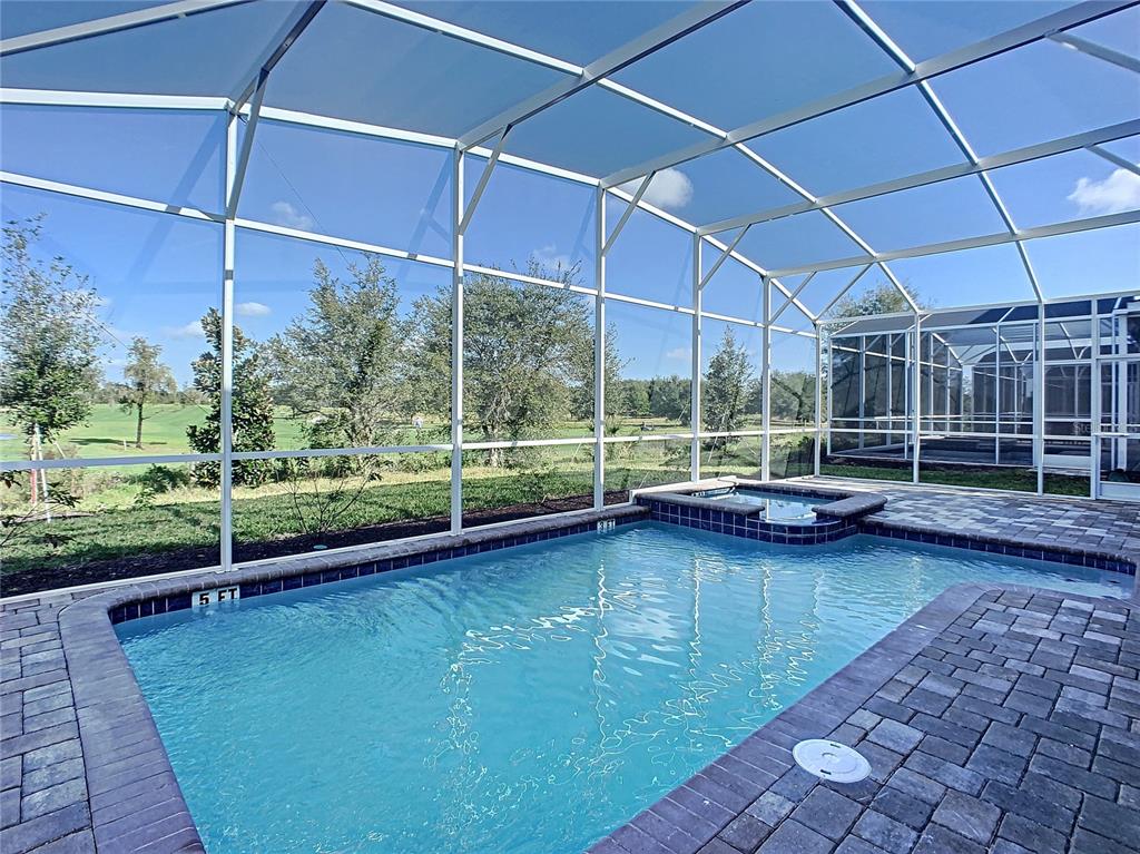 A screened-in swimming pool and spa overlook a grassy golf course on a sunny day — 8841 CRUDEN BAY COURT, DAVENPORT, FL