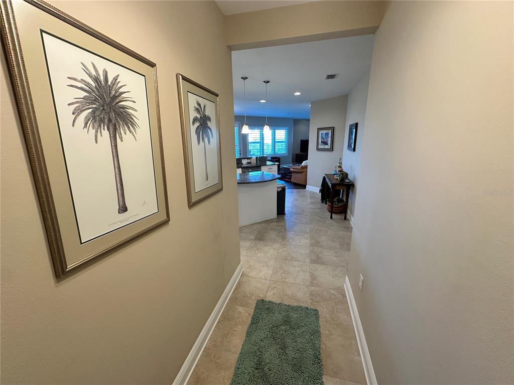 A hallway with framed palm tree art leads into an open-concept kitchen and living area — 7740 34TH AVE W UNIT 202, BRADENTON, FL