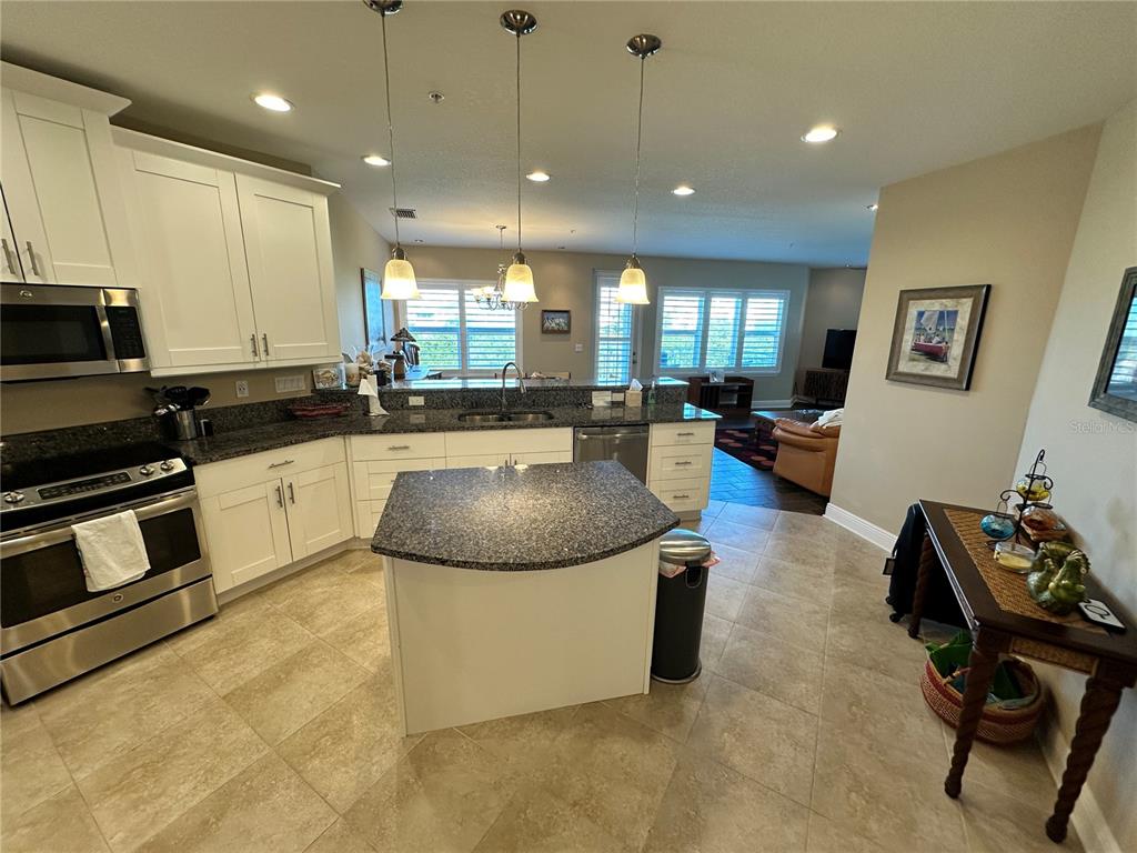 A kitchen features white cabinets, granite countertops, a central island, and tile flooring — 7740 34TH AVE W UNIT 202, BRADENTON, FL