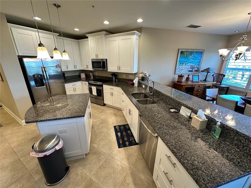 A kitchen features white cabinets, dark granite countertops, stainless steel appliances, and a center island — 7740 34TH AVE W UNIT 202, BRADENTON, FL