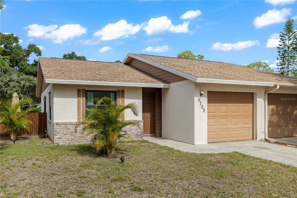 A single-story house with a tan stucco exterior, a brown garage door, and a shingled roof — 5723 DEER HOLLOW TRAIL, SARASOTA, FL
