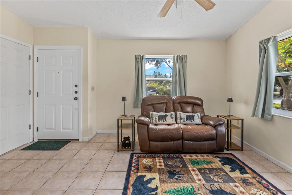 A living room features tile flooring, a brown leather loveseat, and a bear-themed area rug — 5723 DEER HOLLOW TRAIL, SARASOTA, FL
