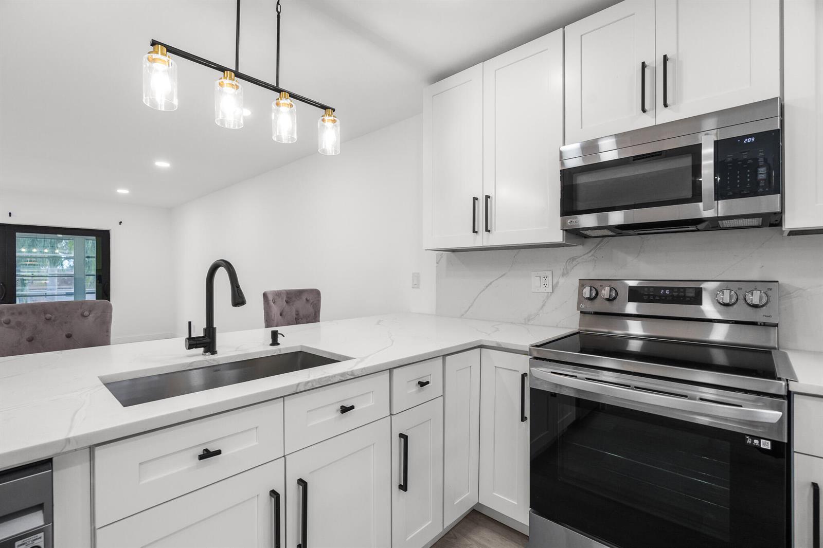 A modern kitchen features white cabinets, stainless steel appliances, and a marble-look countertop with sink — 5 Abbey Lane # 207, Delray Beach FL 33446, DELRAY BEACH, FL