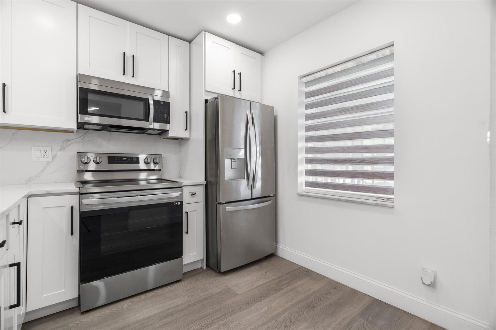 A kitchen features white cabinets, stainless steel appliances, marble-look backsplash, and wood-style flooring — 5 Abbey Lane # 207, Delray Beach FL 33446, DELRAY BEACH, FL