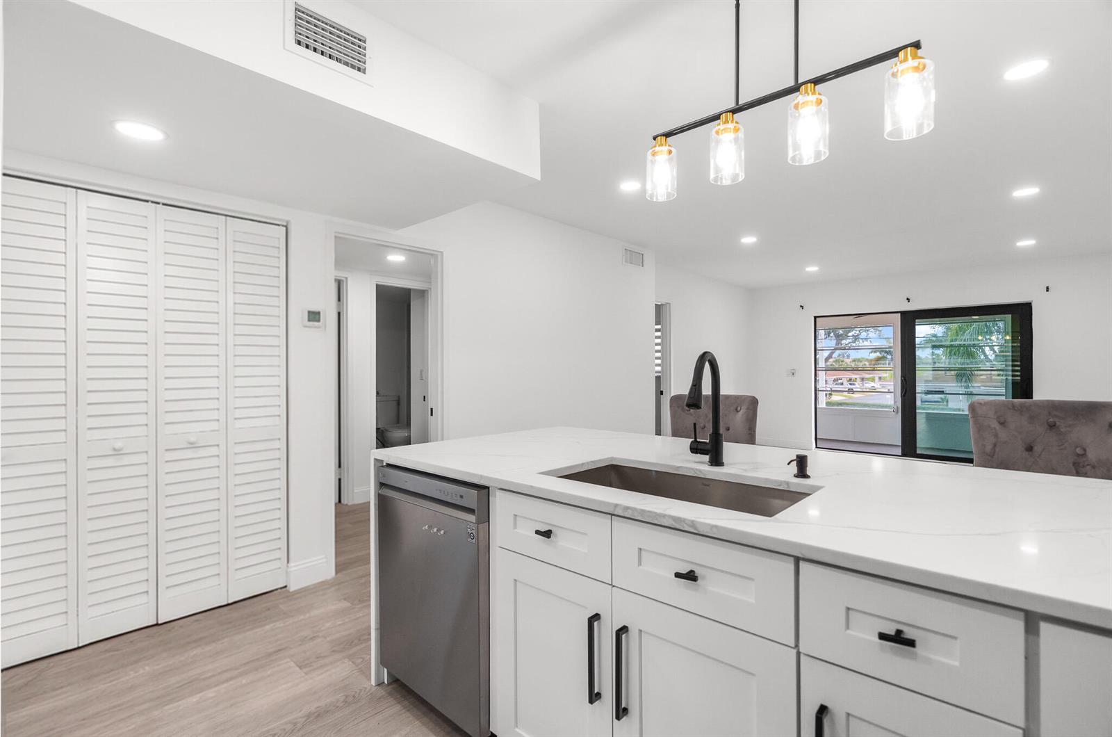 A modern kitchen island with a stainless steel sink and dishwasher faces a living area — 5 Abbey Lane # 207, Delray Beach FL 33446, DELRAY BEACH, FL