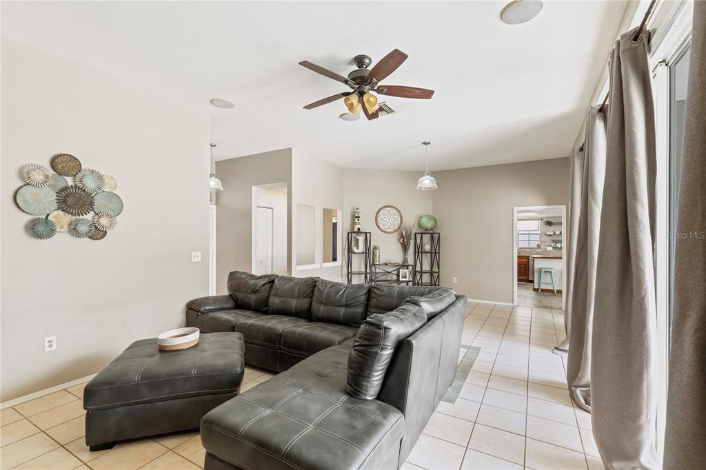 A living room features a large grey sectional sofa, tile flooring, and a ceiling fan — 1690 WINNERS CIRCLE, TARPON SPRINGS, FL