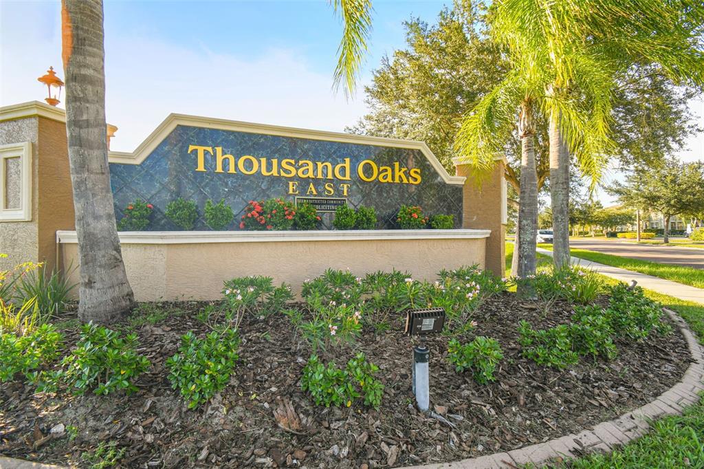 A sign for Thousand Oaks East stands in a landscaped garden with palm trees — 1616 REGAL MIST LOOP, TRINITY, FL