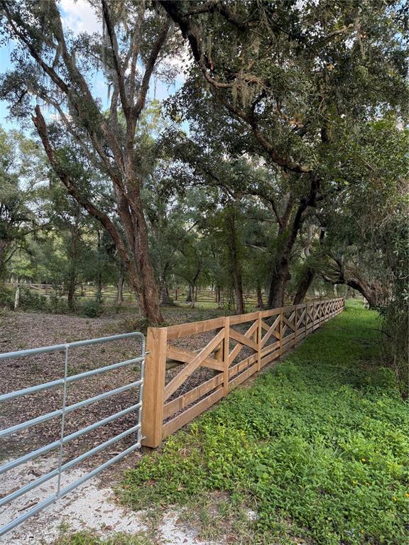 A metal gate connects to a wooden cross-buck fence bordering a wooded property — SE BROWN ROAD, ARCADIA, FL