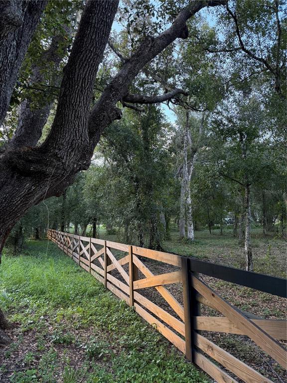 A wooden cross-buck fence runs along the edge of a wooded lot with large trees — SE BROWN ROAD, ARCADIA, FL