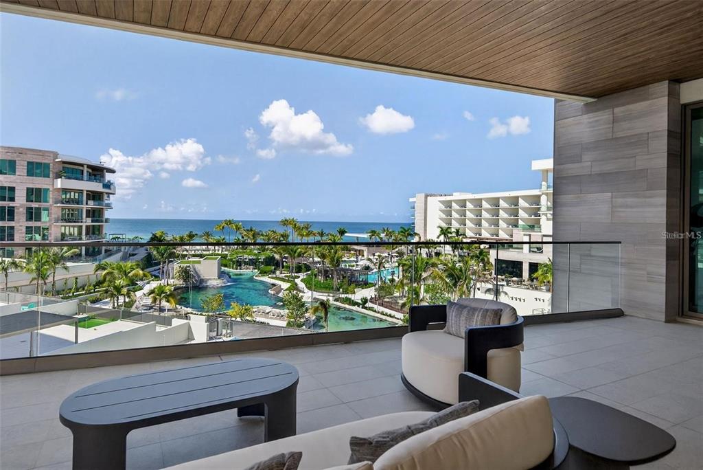 A modern balcony features outdoor seating overlooking a resort pool and the ocean — 1591 GULF OF MEXICO DRIVE UNIT 410, LONGBOAT KEY, FL