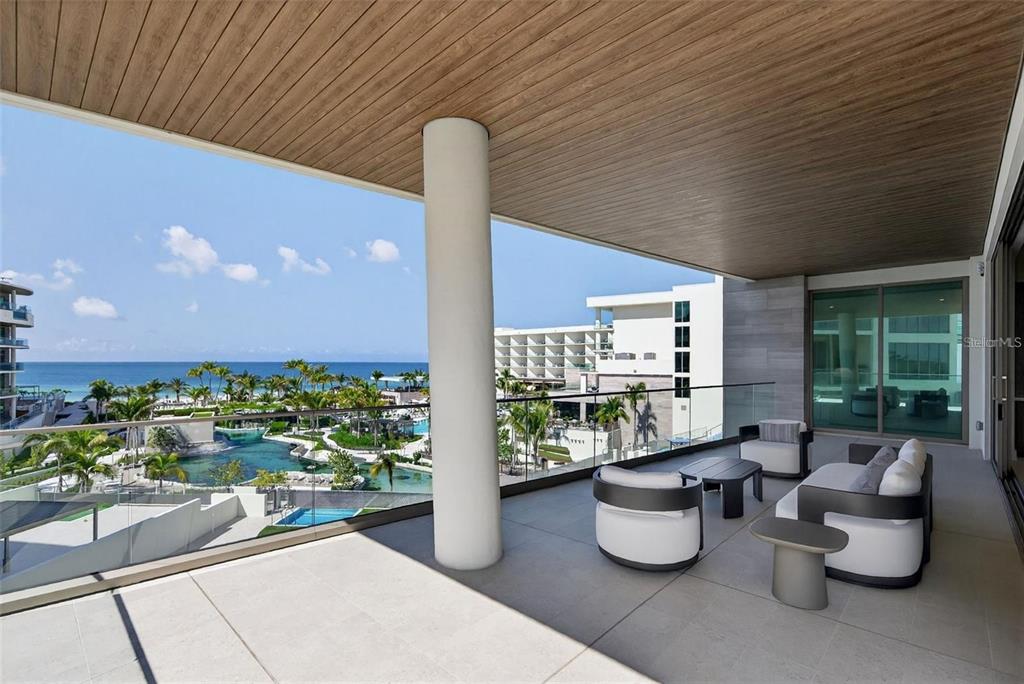 A spacious balcony features modern outdoor furniture, a large support column, and a coastal view — 1591 GULF OF MEXICO DRIVE UNIT 410, LONGBOAT KEY, FL