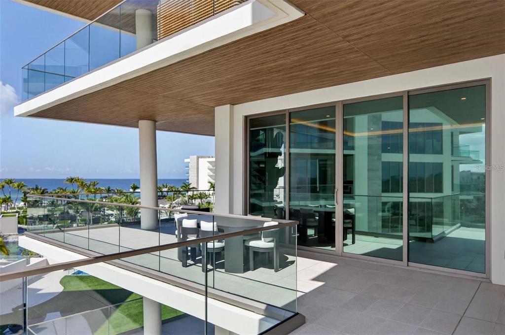 A modern balcony features a glass railing, outdoor dining set, and views of the ocean — 1591 GULF OF MEXICO DRIVE UNIT 410, LONGBOAT KEY, FL