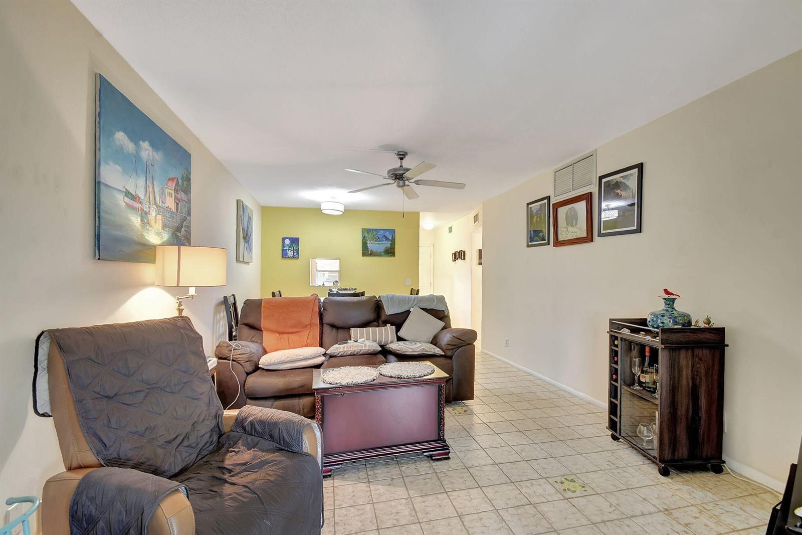 A living room features tile flooring, a brown sofa, a recliner, and wall-mounted artwork — 2121 NE 1st Court # 105, Boynton Beach FL 33435, BOYNTON BEACH, FL