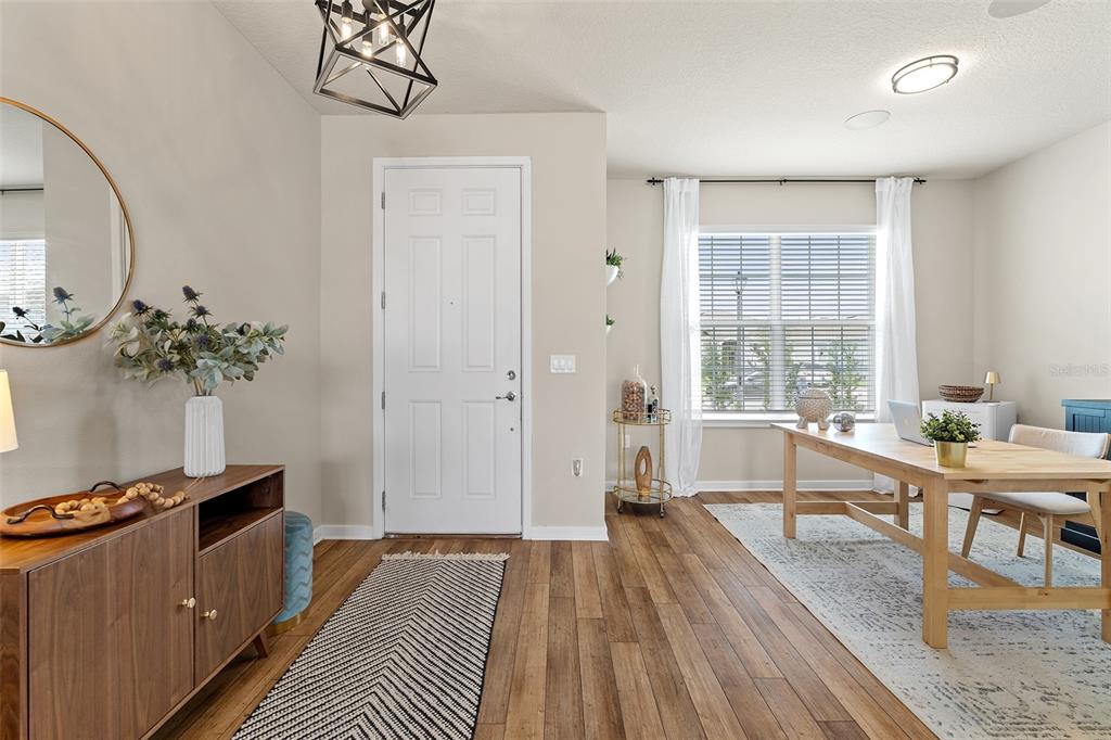 A bright home office features wood-look flooring, a wooden desk, and a white front door — 1444 GRAND PALM DRIVE, ORLANDO, FL