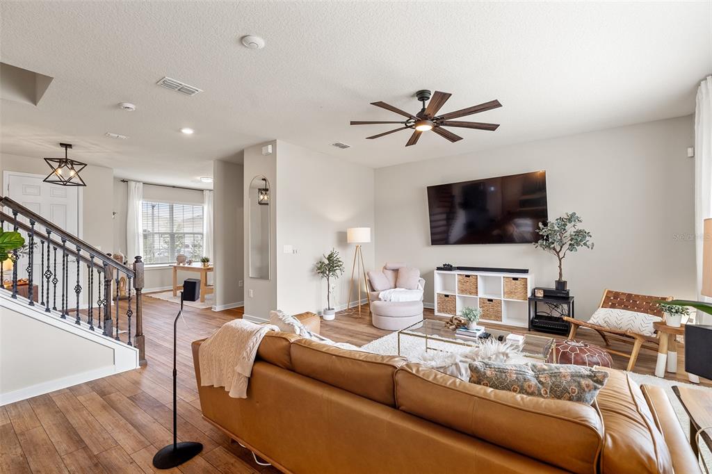 A living room features a leather sofa, a wall-mounted television, and a wooden staircase — 1444 GRAND PALM DRIVE, ORLANDO, FL