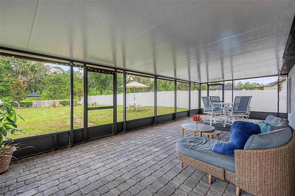 A covered patio with a paver floor and screen walls overlooks a fenced backyard — 13411 WILLOW BLUESTAR LOOP, RIVERVIEW, FL