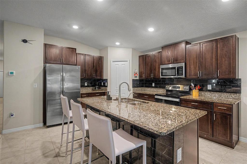A kitchen features dark wood cabinets, granite countertops, a center island, and stainless steel appliances — 13411 WILLOW BLUESTAR LOOP, RIVERVIEW, FL