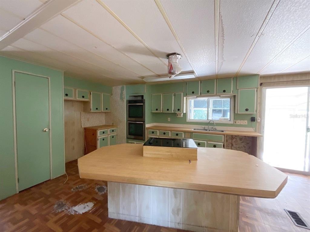 A kitchen with green cabinets, a central island, wood-look flooring, and a double wall oven — 12830 SE 7TH STREET, SILVER SPRINGS, FL