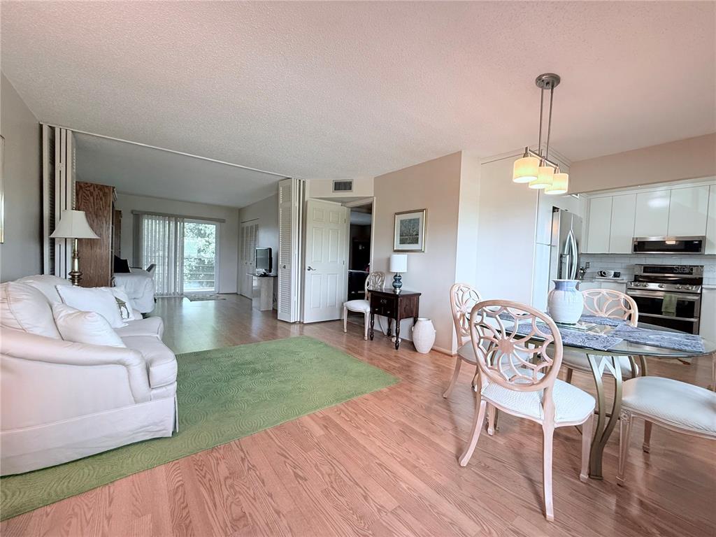 An open-concept living and dining area features light wood flooring, a green rug, and kitchen — 4460 IRONWOOD CIRCLE UNIT 304A, BRADENTON, FL