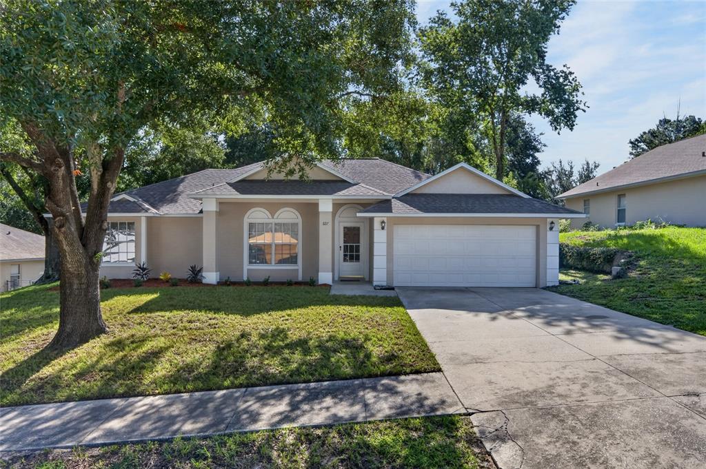A single-story suburban house with a tan exterior, white trim, and a two-car garage — 827 FORESTWOOD DRIVE, MINNEOLA, FL