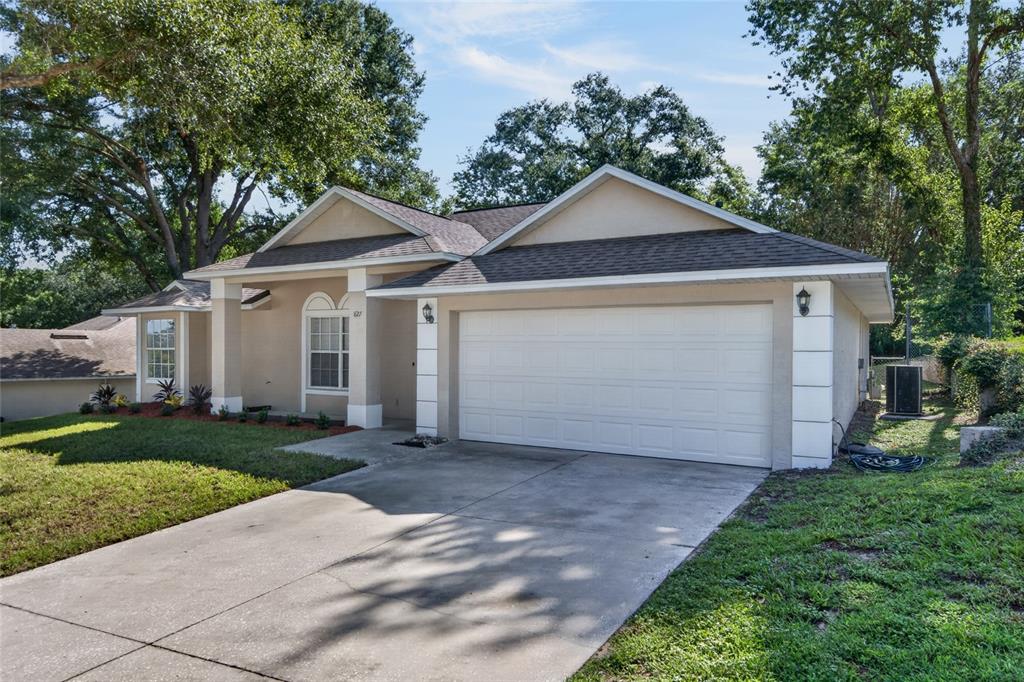 A single-story house with a beige stucco exterior, a two-car garage, and a concrete driveway — 827 FORESTWOOD DRIVE, MINNEOLA, FL