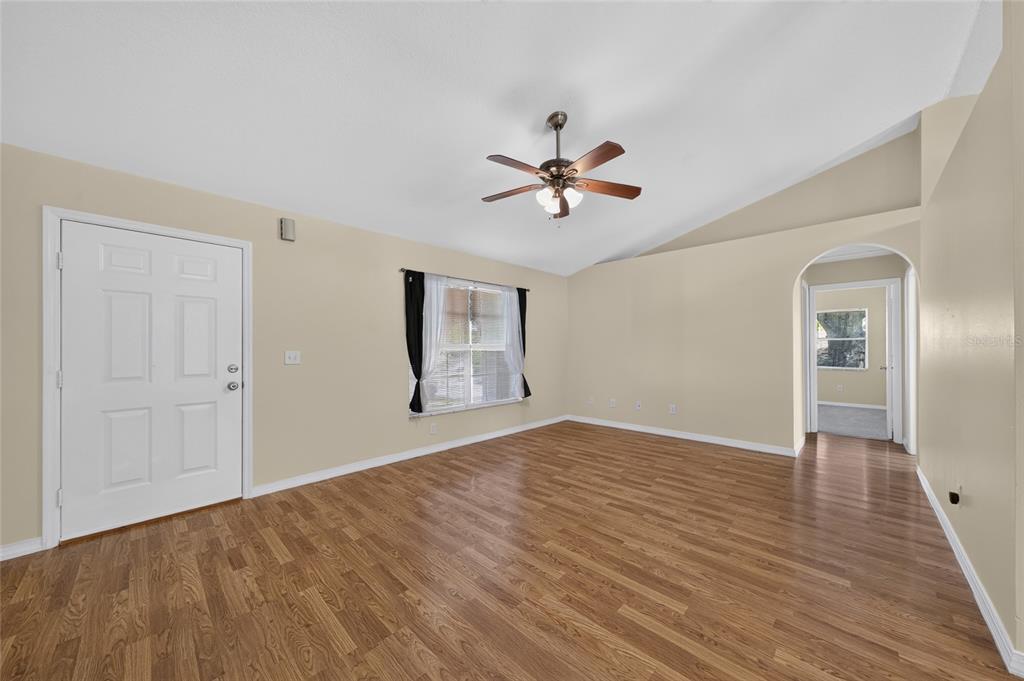 An empty living room with wood-look flooring, a ceiling fan, and an arched doorway — 827 FORESTWOOD DRIVE, MINNEOLA, FL