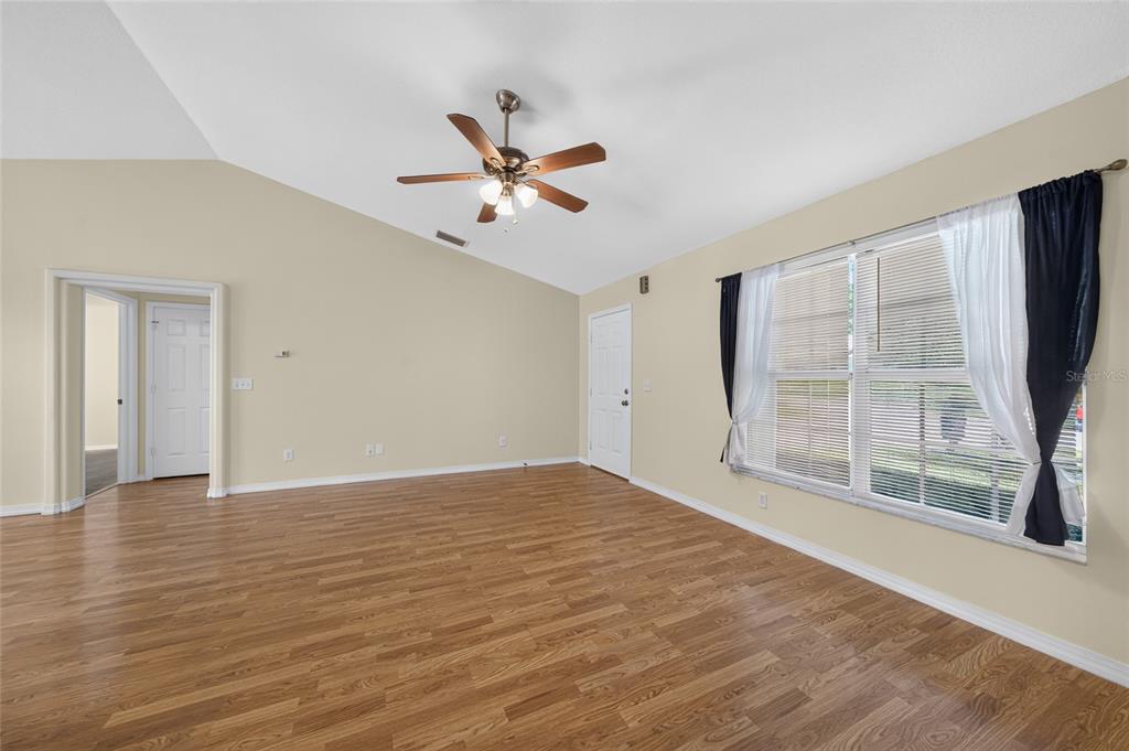 An empty living room features wood-look flooring, a vaulted ceiling with a fan, and windows — 827 FORESTWOOD DRIVE, MINNEOLA, FL