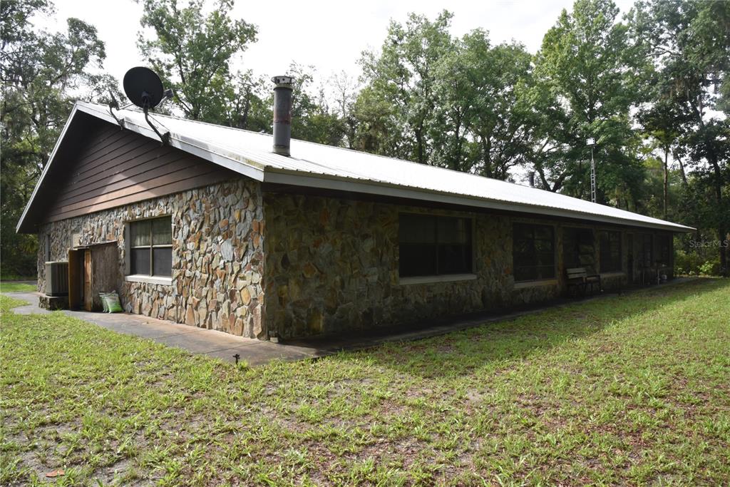 A single-story house with a stone exterior, metal roof, and a surrounding concrete walkway — 8650 NW 136TH AVENUE, CHIEFLAND, FL