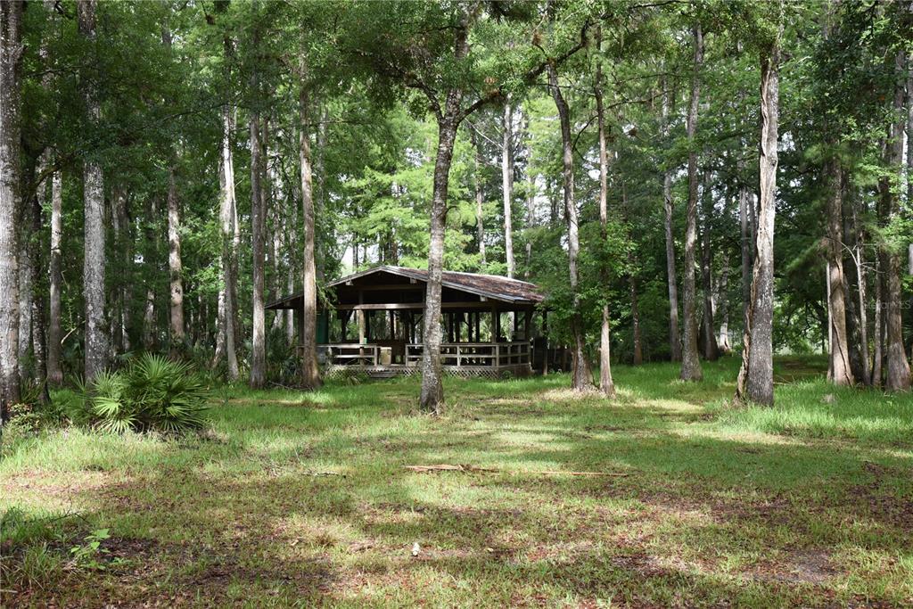 A wooden pavilion with a porch sits in a clearing surrounded by tall trees — 8650 NW 136TH AVENUE, CHIEFLAND, FL