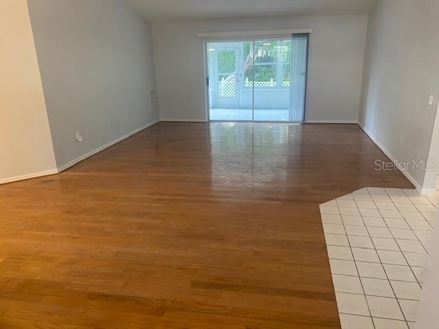 An empty living room features hardwood floors, a tiled entryway, and sliding glass patio doors — 7050 WOODIBIS DRIVE, NEW PORT RICHEY, FL